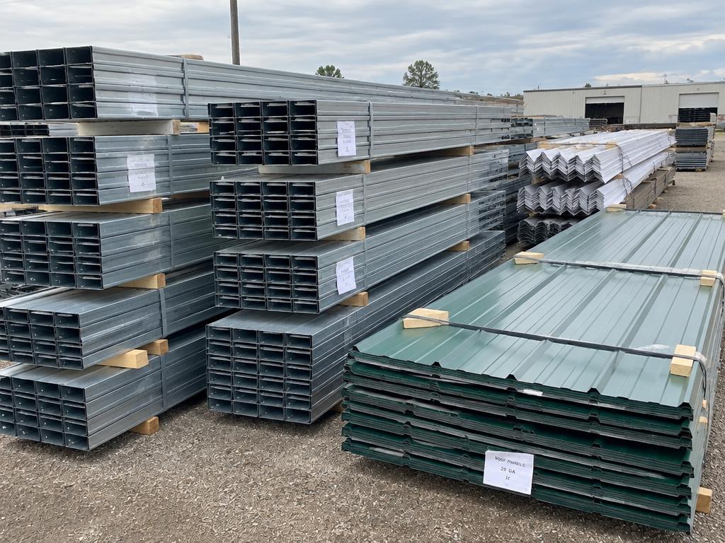 Bundles of steel purlins, trim, and metal roof panels stacked in a yard